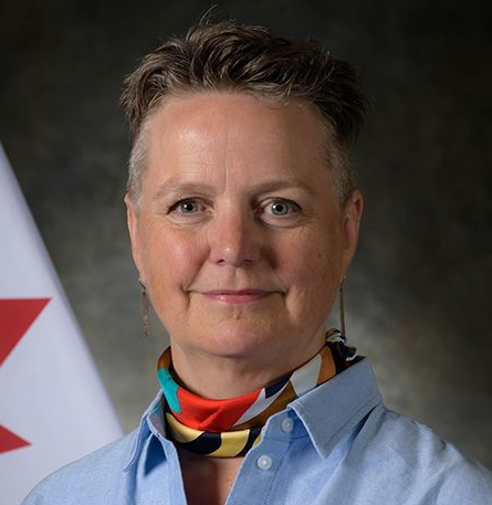 Woman wearing glasses smiles at the camera, wearing a blazer and white shirt.