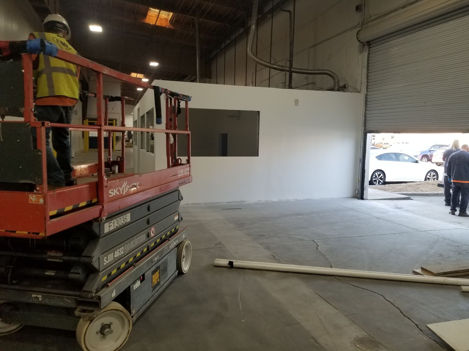 A man is standing on a scissor lift in a warehouse.