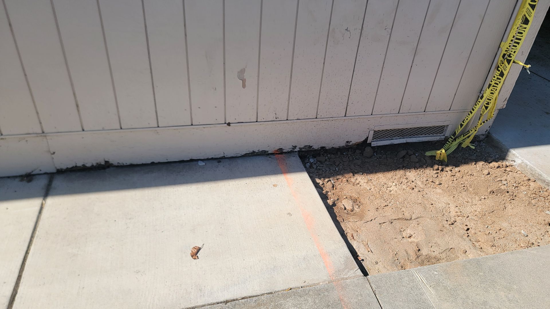A white fence is sitting on a sidewalk next to a yellow tape.