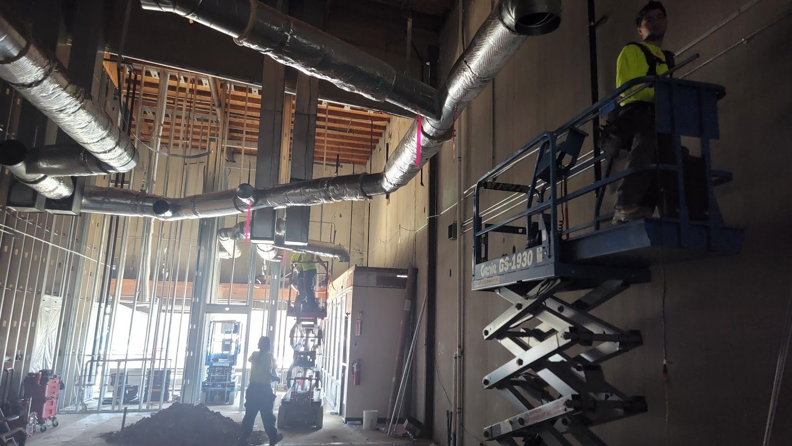 A man is standing on a scissor lift in a building under construction.