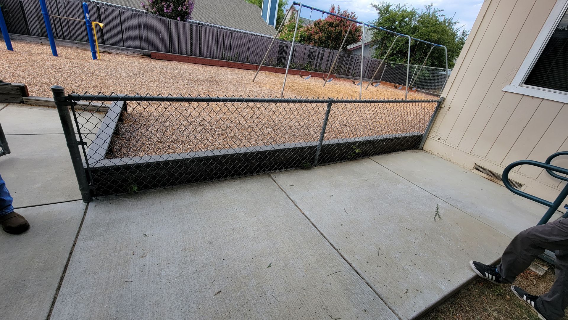 A concrete patio with a chain link fence and a playground in the background.