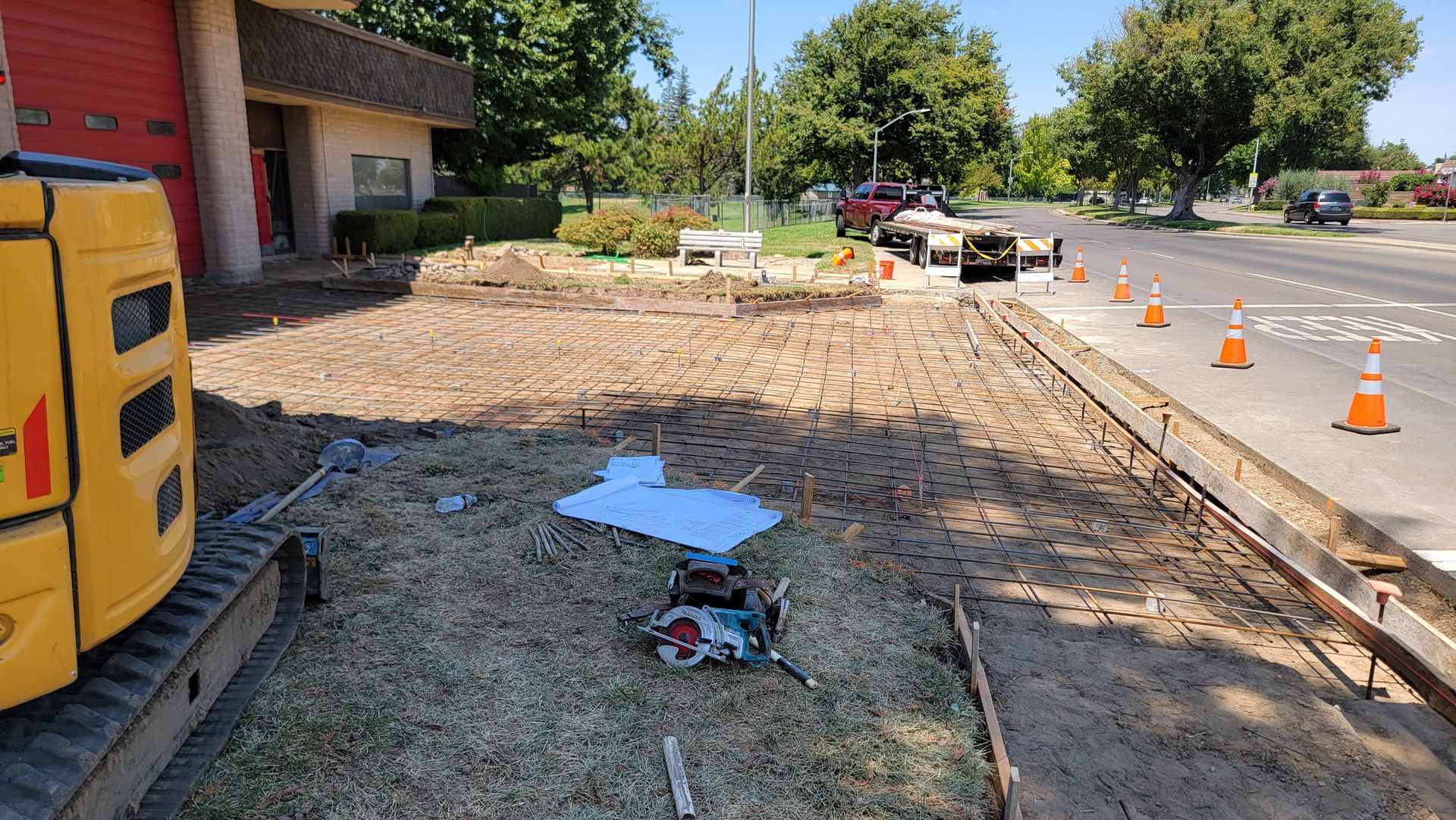 A yellow excavator is sitting on the side of a road next to a building.