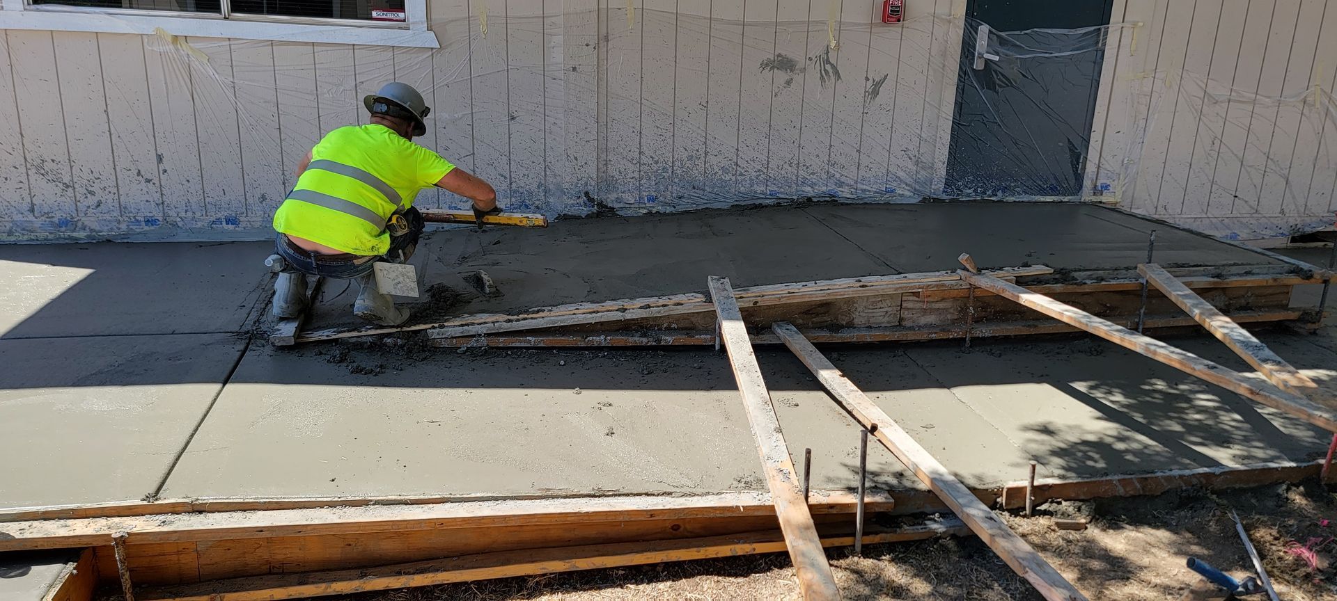 A construction worker is pouring concrete on a sidewalk in front of a building.