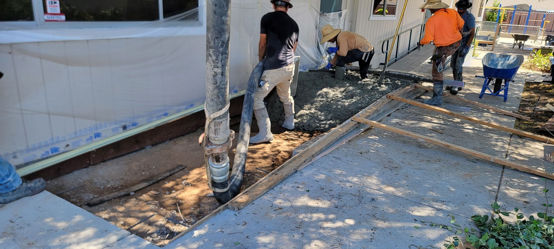 A group of construction workers are working on a sidewalk in front of a house.