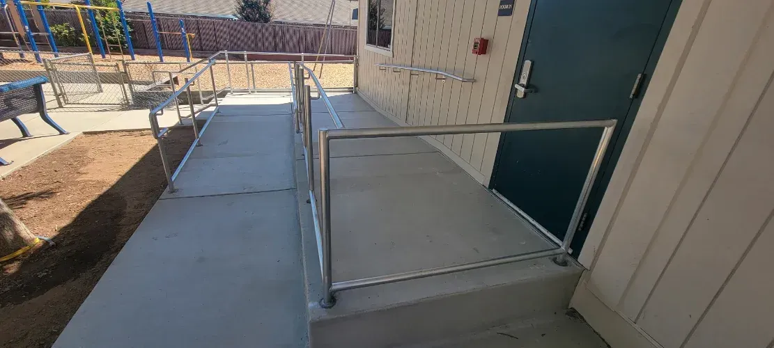 A concrete ramp with a metal railing leading to a door.