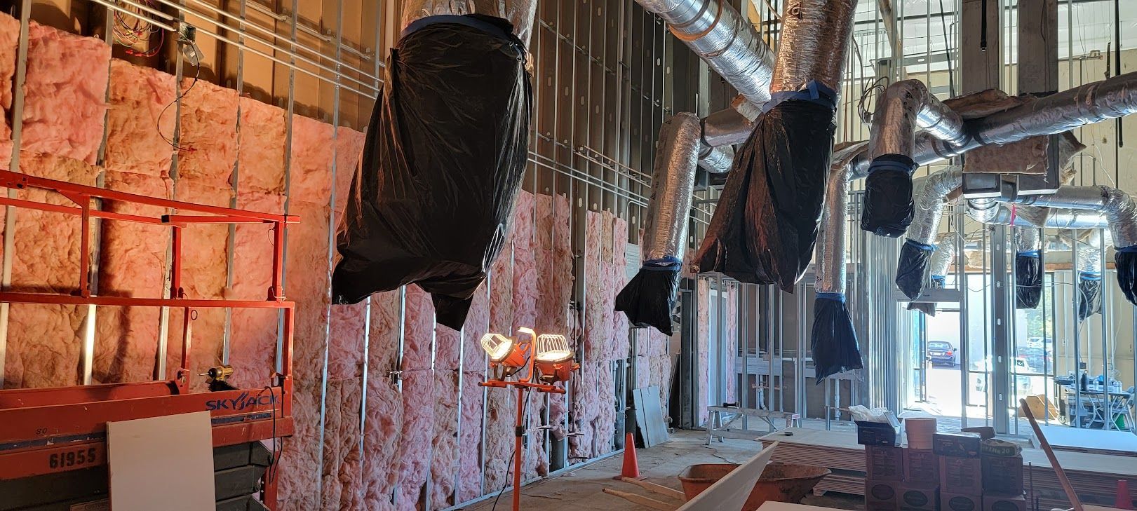 A large room is being built with a lot of pipes hanging from the ceiling.