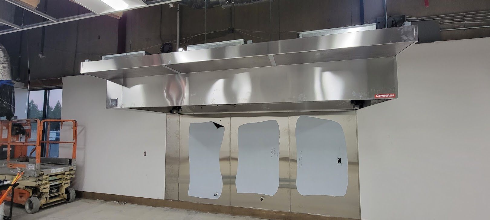 A large stainless steel hood is hanging from the ceiling of a building.