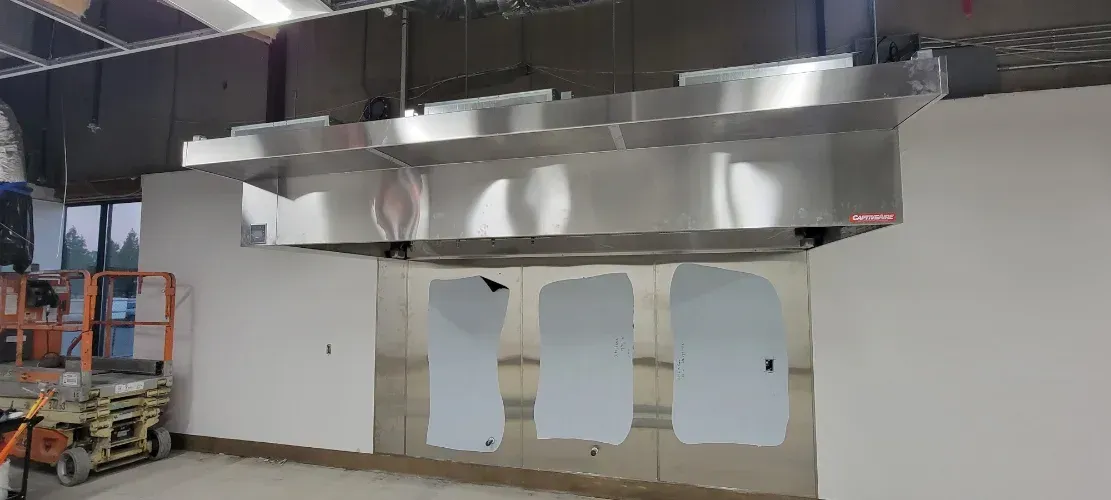 A stainless steel hood is hanging from the ceiling in a kitchen.