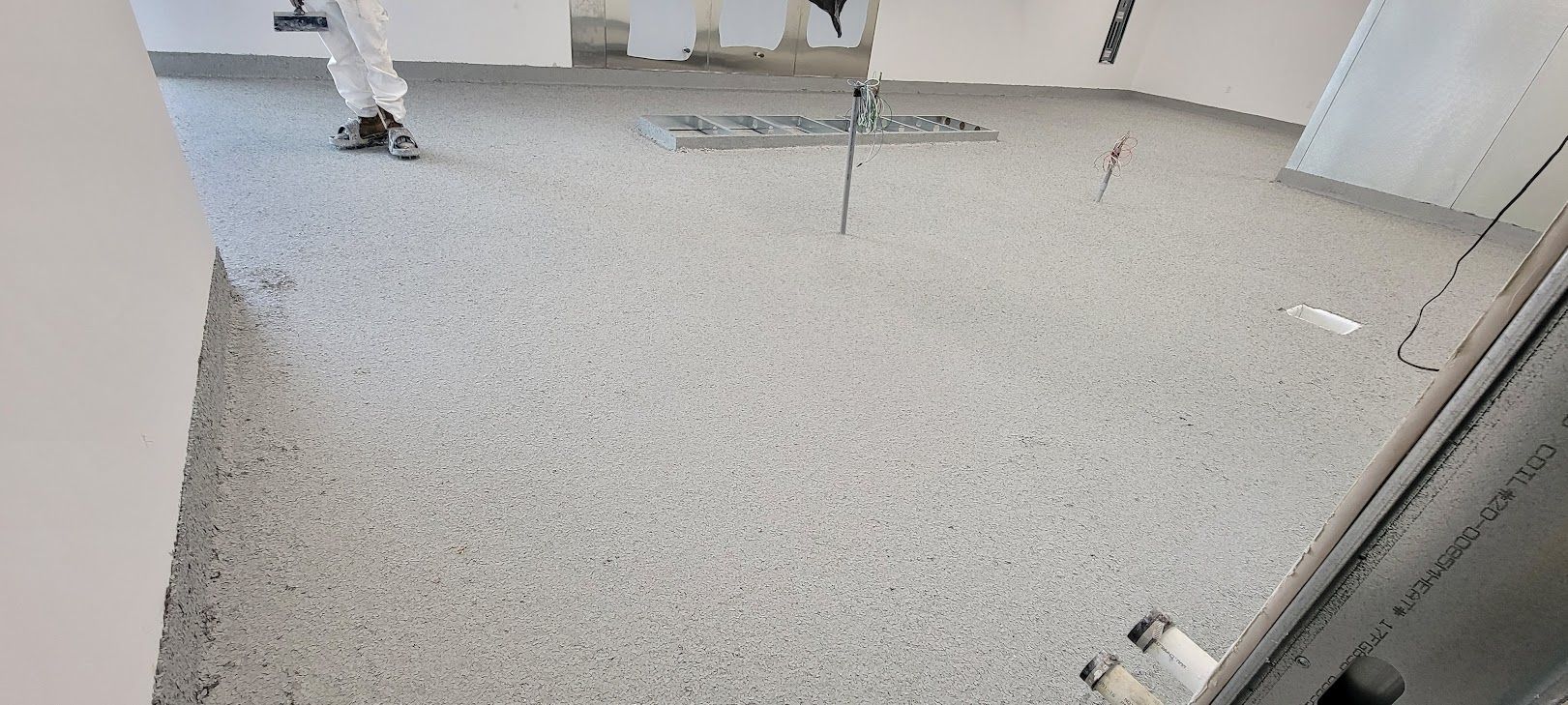A person is laying concrete on a floor in a room.