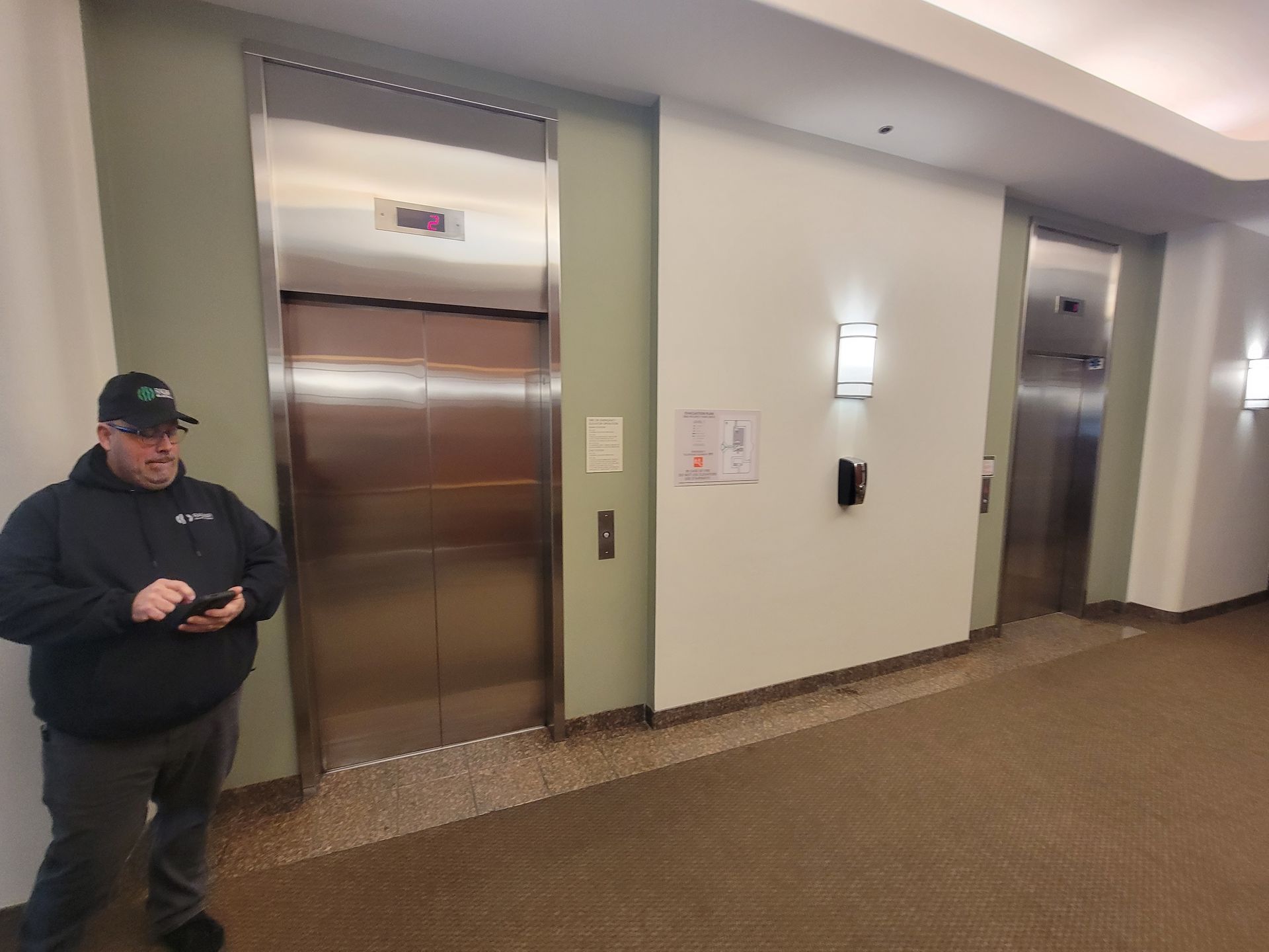 A man is standing in front of an elevator in a hallway.