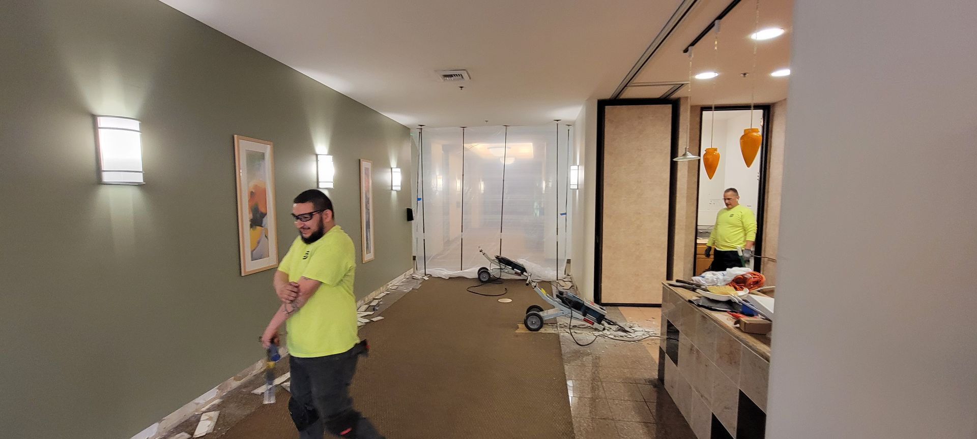 A man in a yellow shirt is cleaning a hallway with a broom.