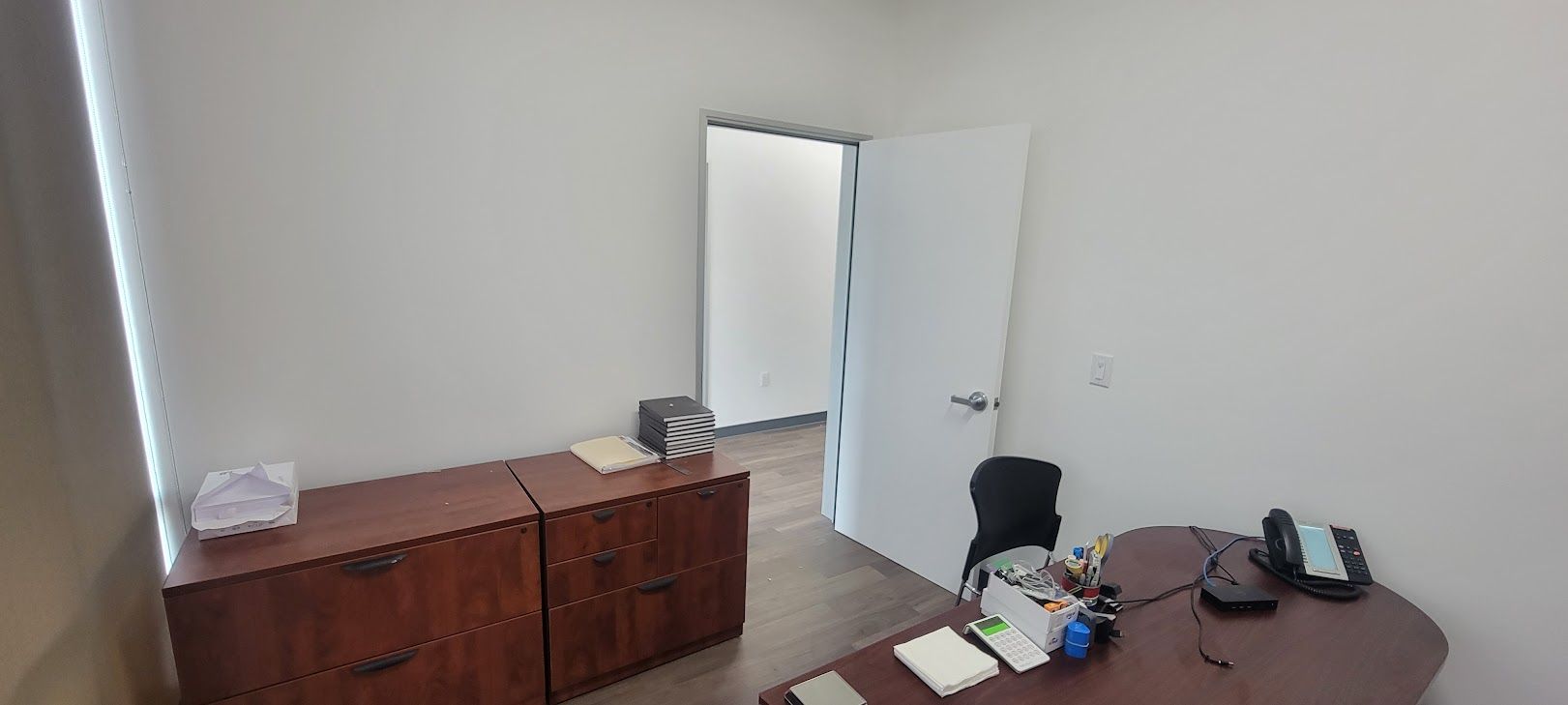 A small office with a desk , chair , filing cabinets and a door.