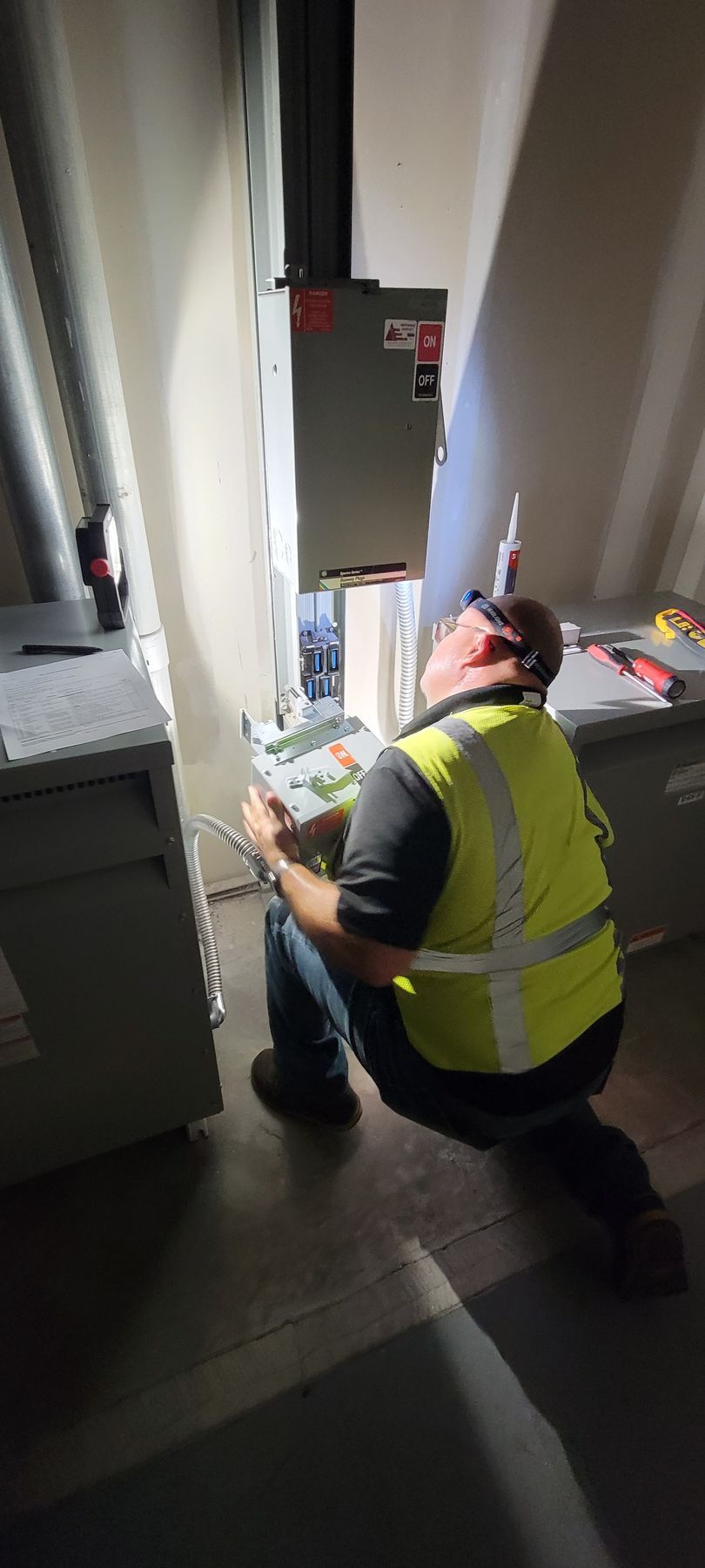 A man in a yellow vest is kneeling down in a dark room looking at a box.