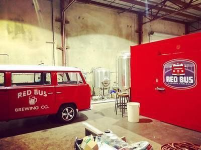 A red bus is parked in a warehouse next to a red wall.