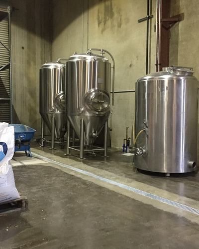 A row of stainless steel tanks are lined up in a room.