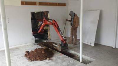 A man is using an excavator to dig a hole in a garage.