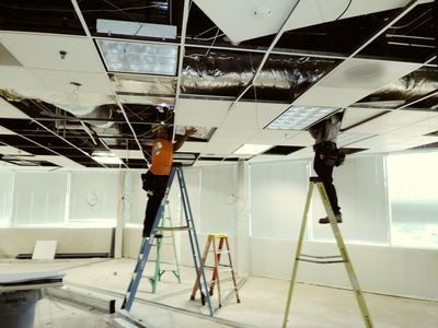 A man standing on a ladder working on a ceiling