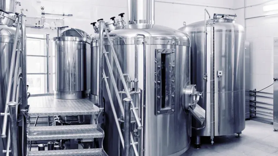 A brewery with a lot of stainless steel tanks and stairs.