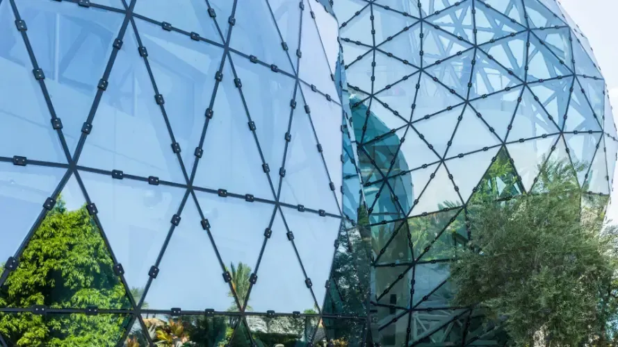 A large glass building with a reflection of trees in the windows.