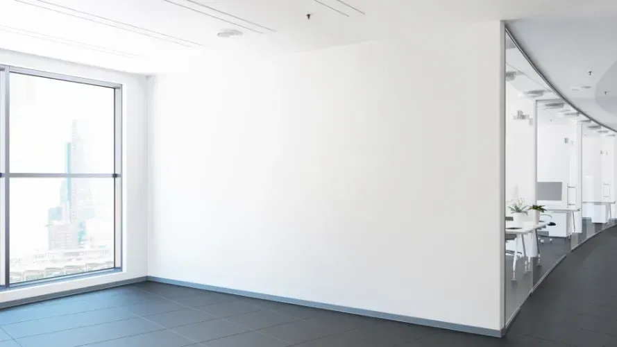An empty office with a large window and a white wall.