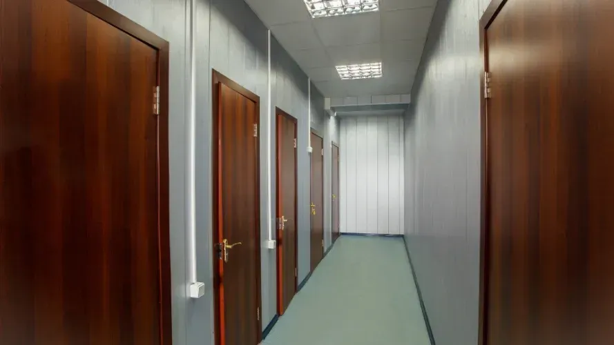 A long hallway with wooden doors and a blue floor.