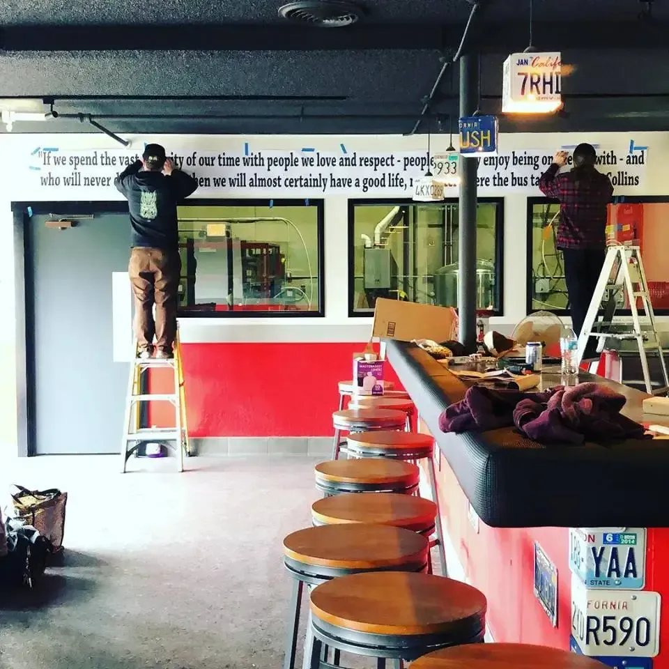 A man standing on a ladder in front of a bar with a license plate that says r590