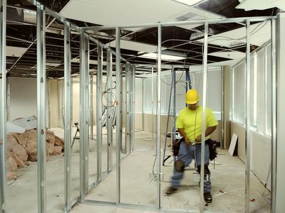 A man in a yellow hard hat is standing in a room under construction.