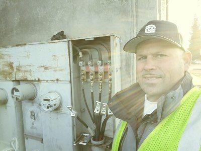 A man wearing a hat and safety vest is standing in front of an electrical box.