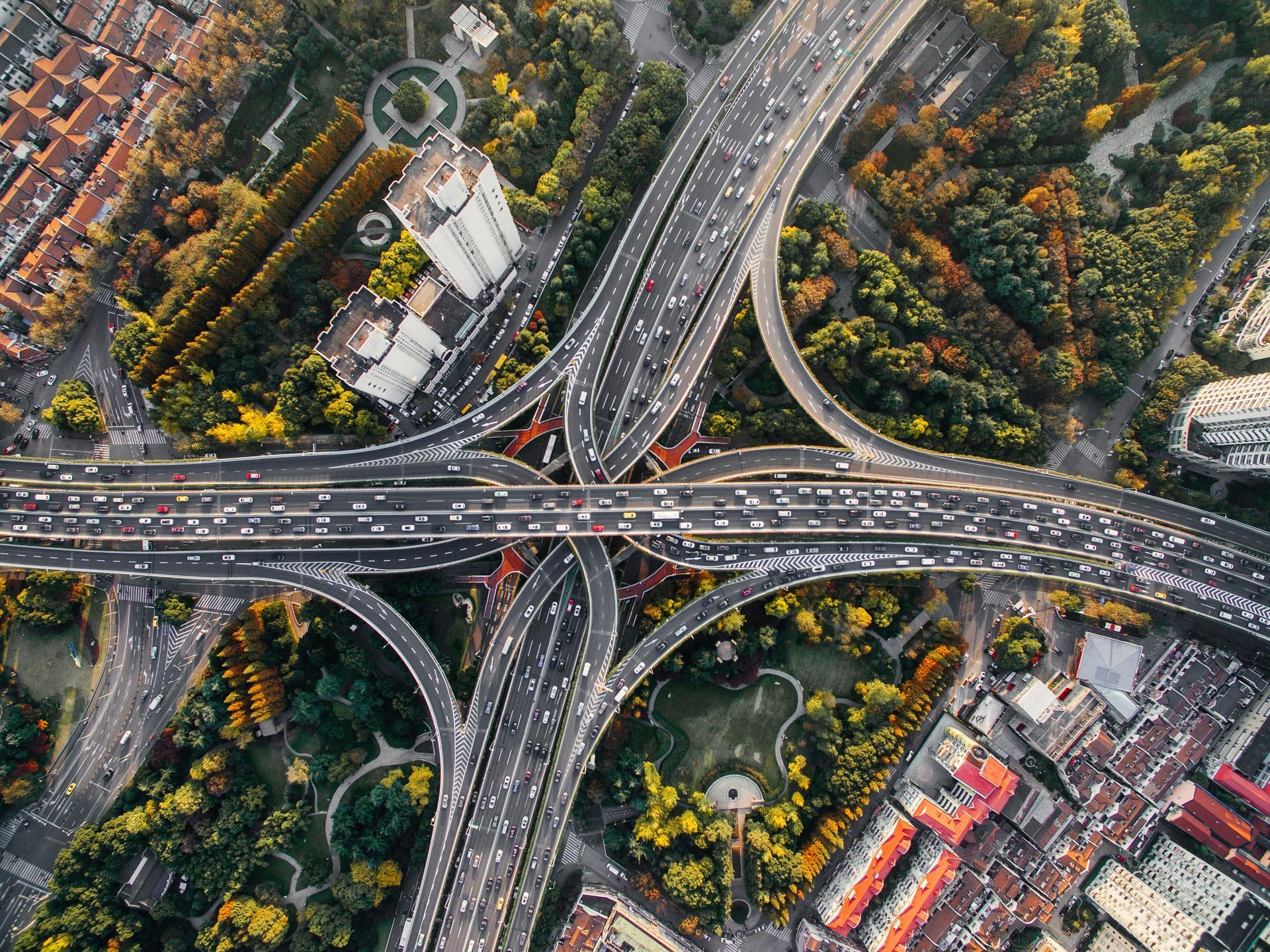 Aerial view of a busy highway interchange cutting through a tree-lined urban area.