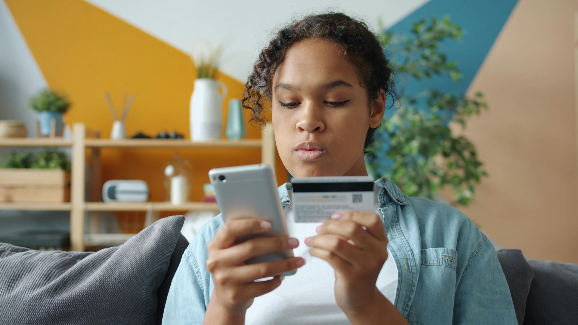 Person using a smartphone and credit card on a couch in a bright living room