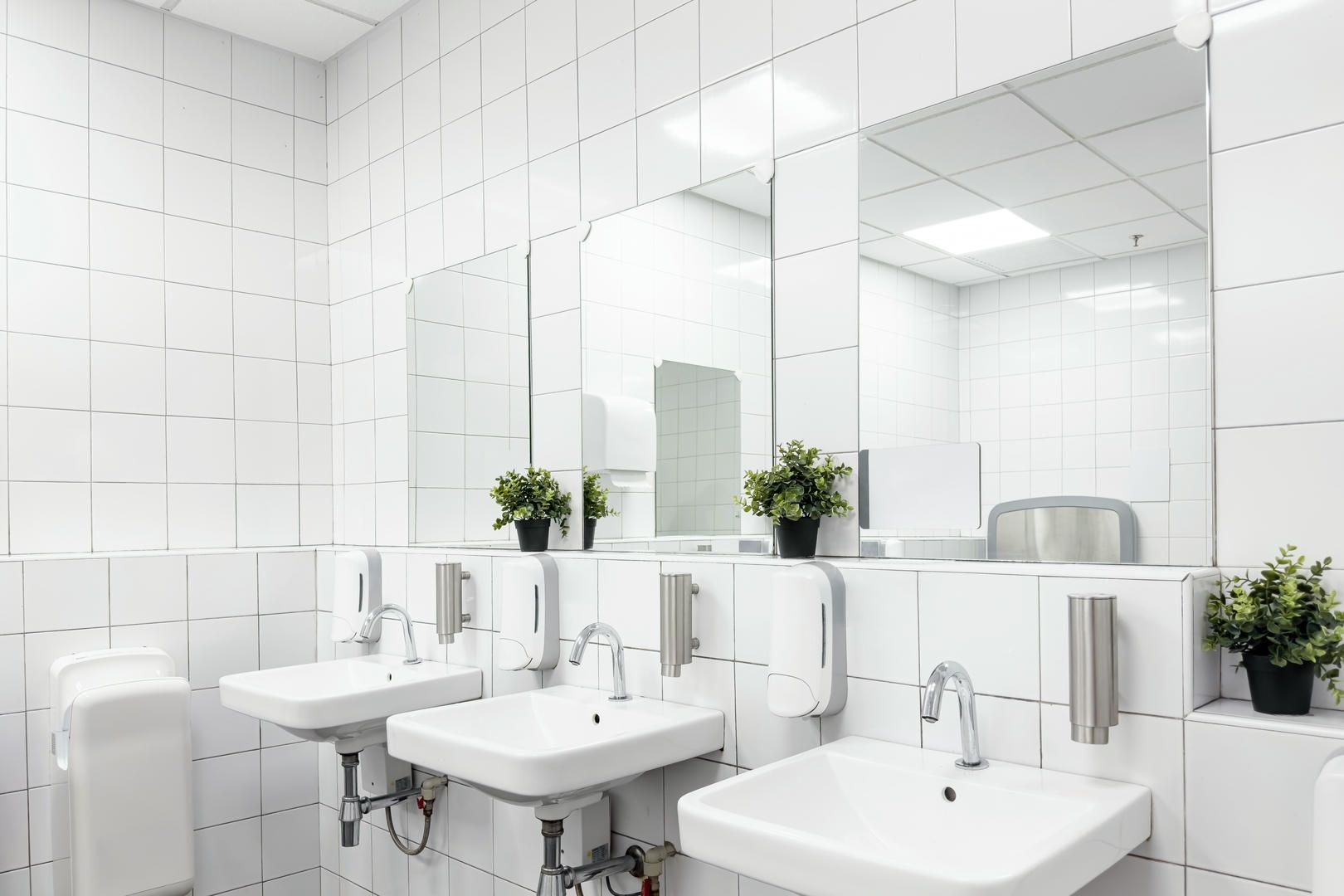 White tiled public restroom with three sinks, mirrors, and hand dryers.