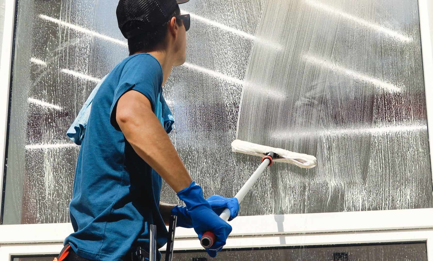 Person wearing blue gloves, cleaning a window with a squeegee.