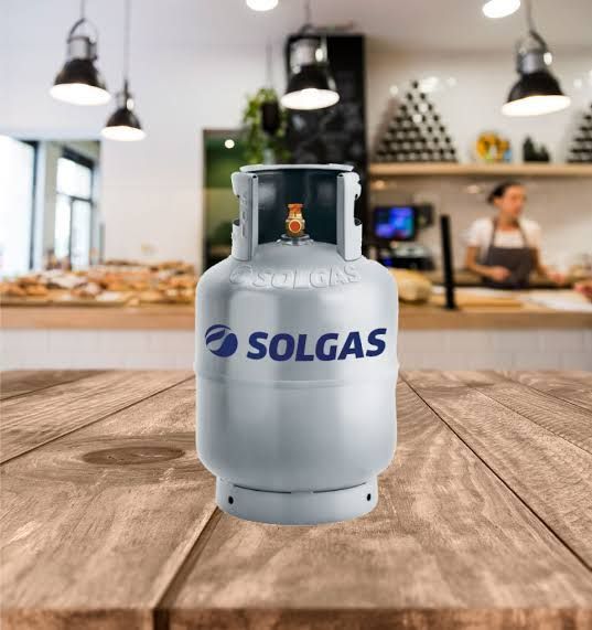 Cilindro de gas Solgas plateado sobre una mesa de madera en un café, con un barista y productos horneados en el fondo.