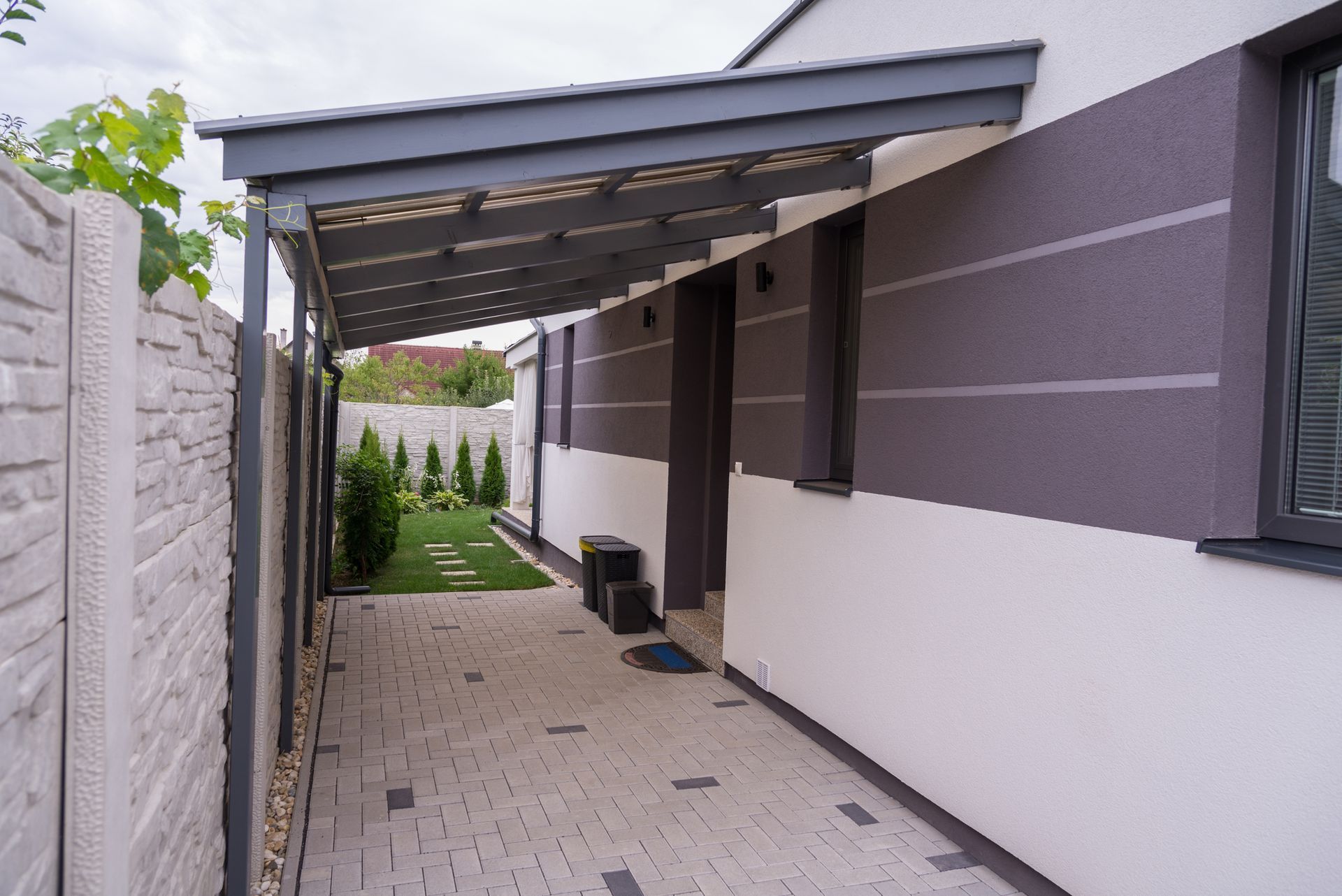 Carport for a small car attached to a house with a corner window, providing weather protection.