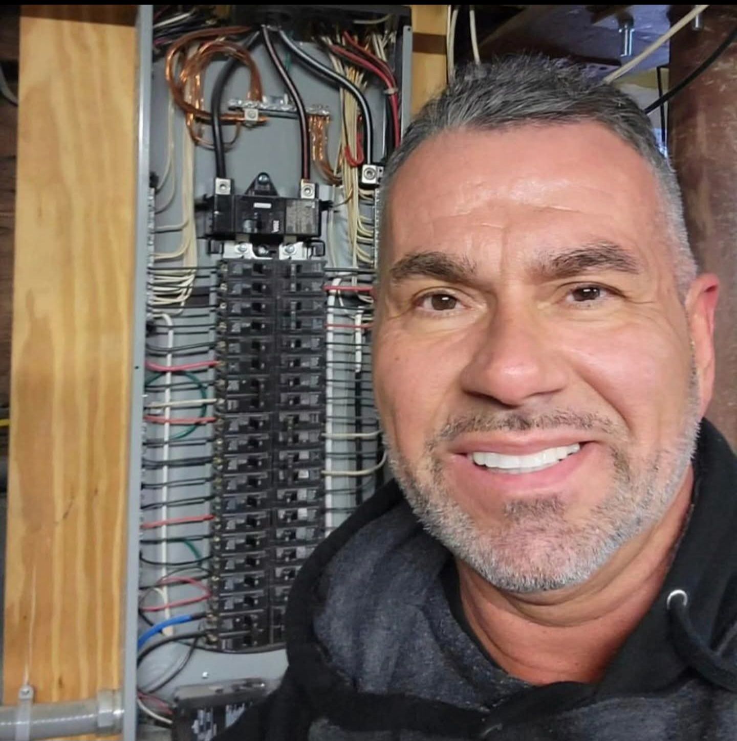 Man smiling in front of an open electrical panel with wires.