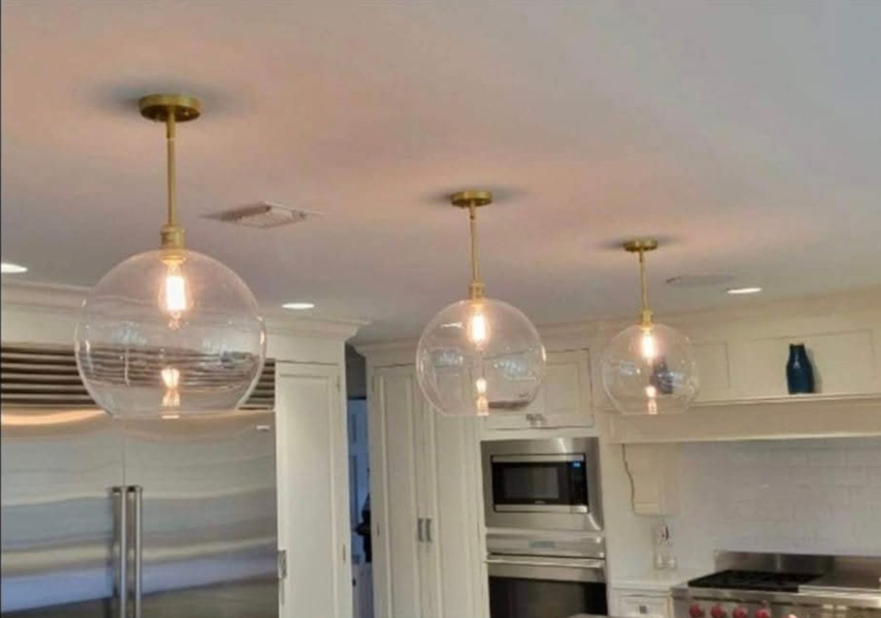 Three clear globe pendant lights with brass fixtures hanging over a white kitchen.