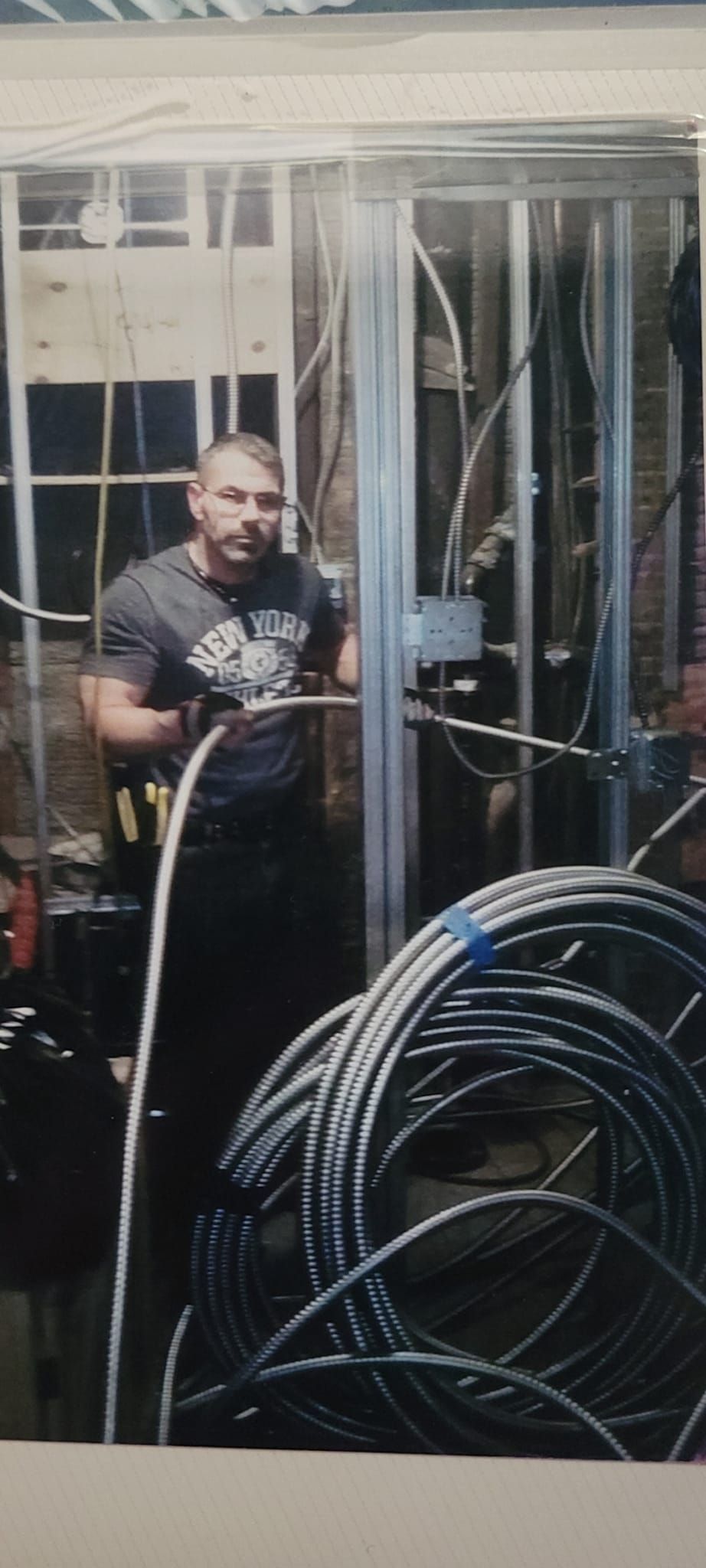 Man holding a cable in a construction setting, near rolled cables.