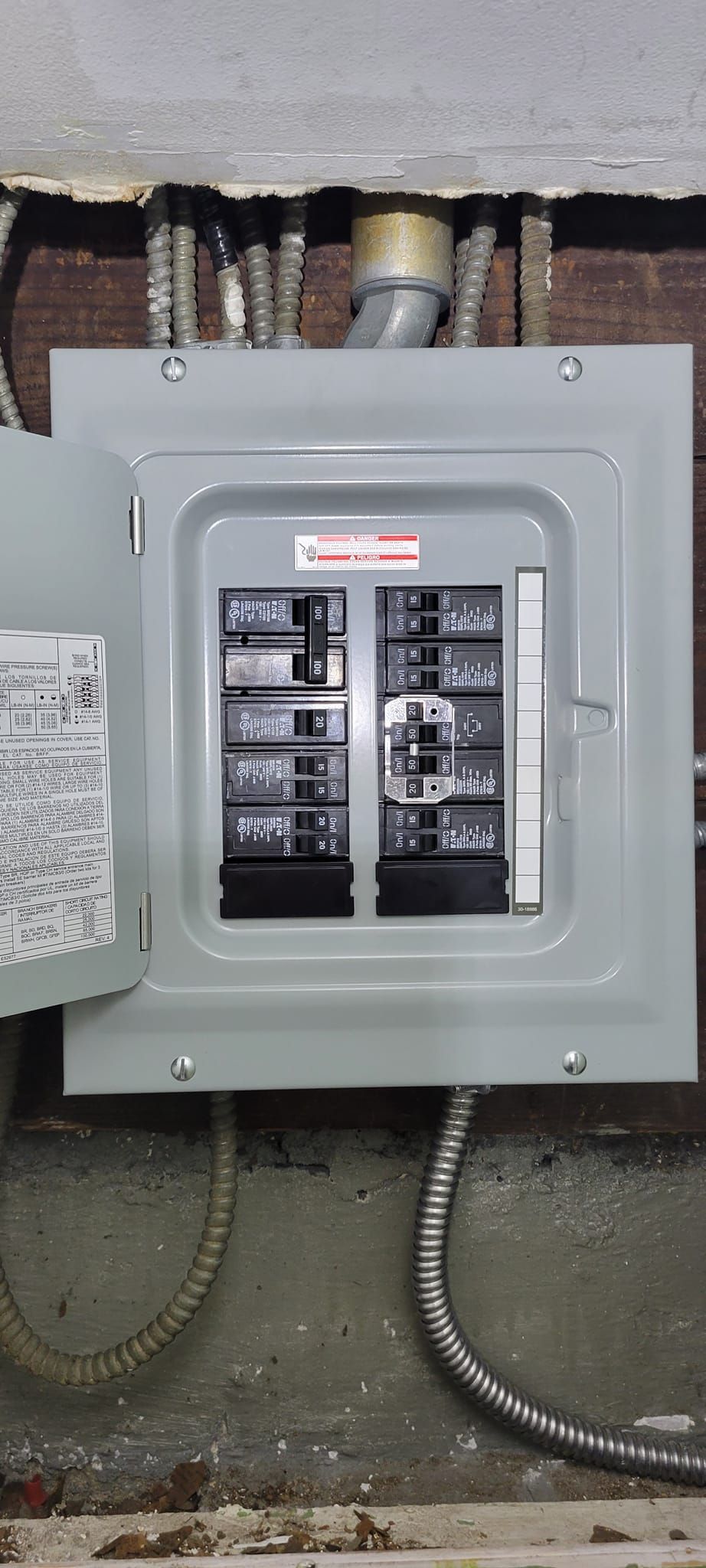 Electrical panel with open door, gray metal, black breakers, mounted on a brick wall, with electrical conduit.