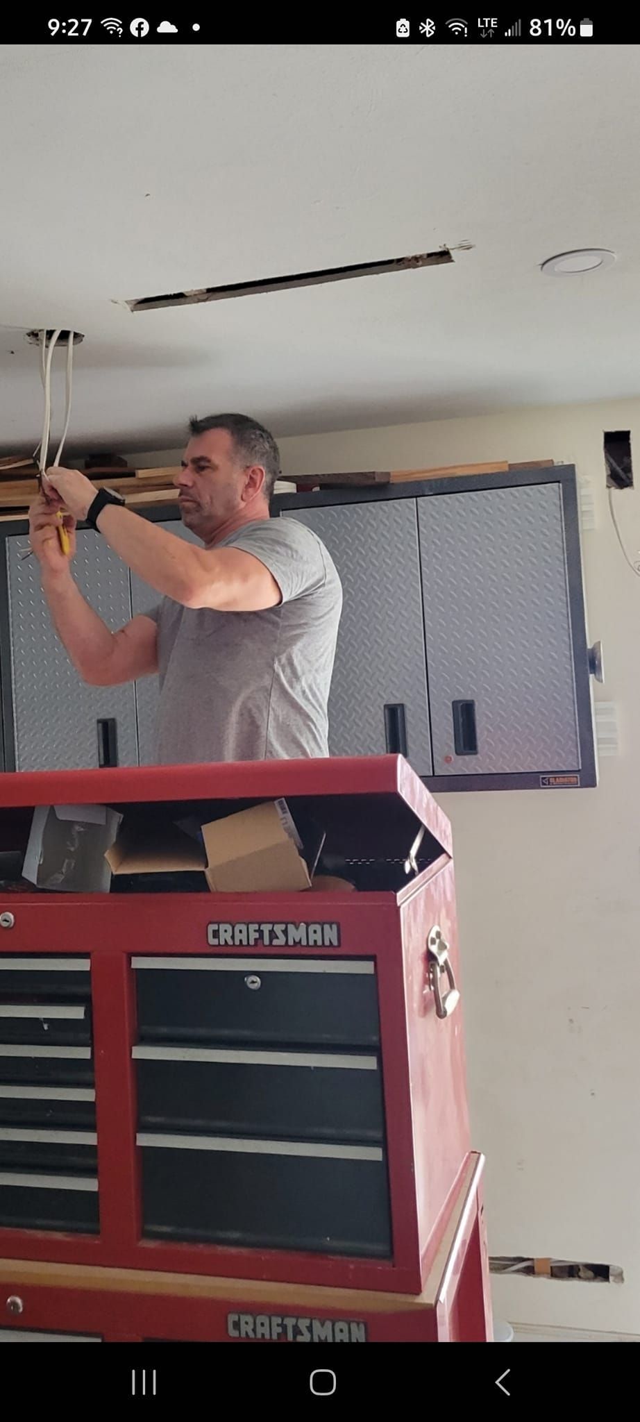Man uses screwdriver to install ceiling light, standing on a red toolbox in a garage.