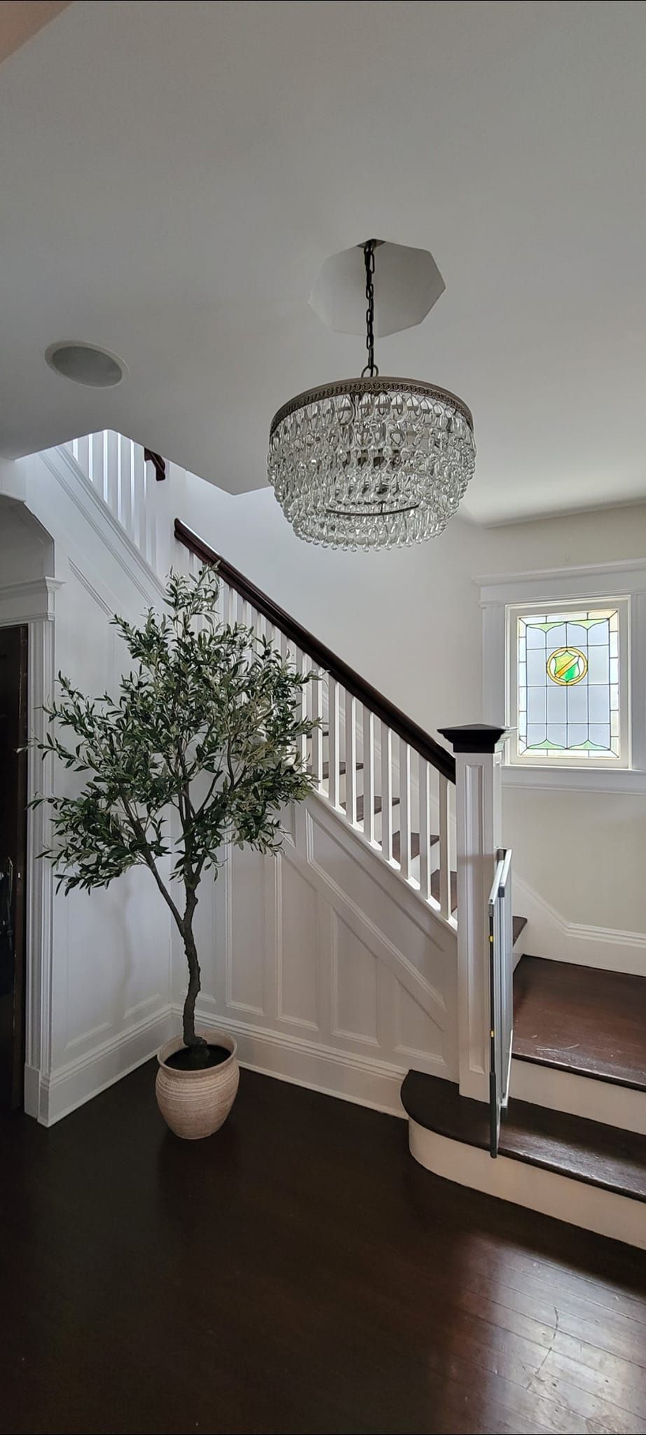 A staircase with white walls and a black banister. A decorative crystal chandelier hangs overhead.