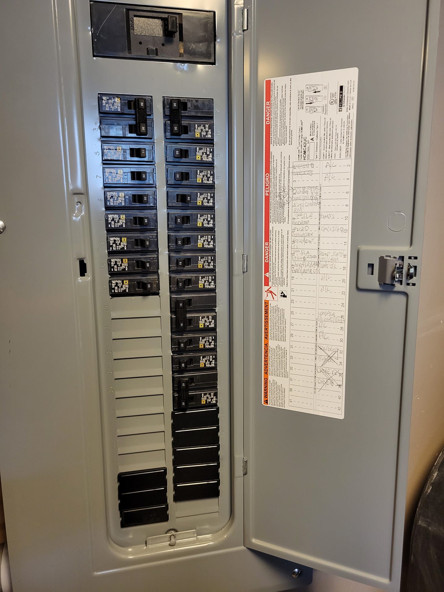 Gray electrical panel with circuit breakers and a diagram on the open door.