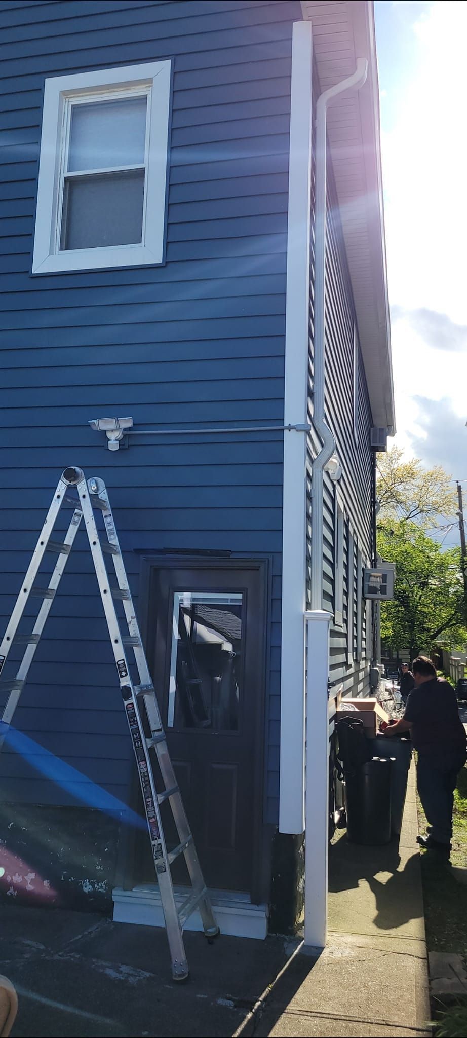 Side of blue house with white trim, a ladder, and people working outside.