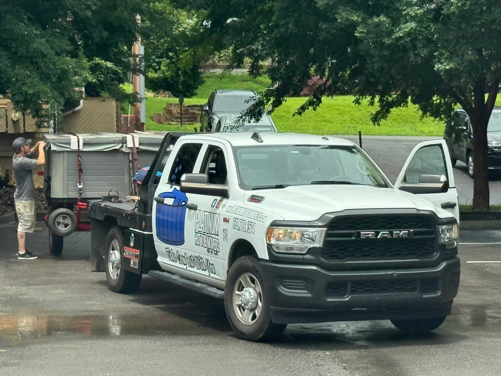 White RAM truck with trailer parked on wet asphalt; man standing by trailer.