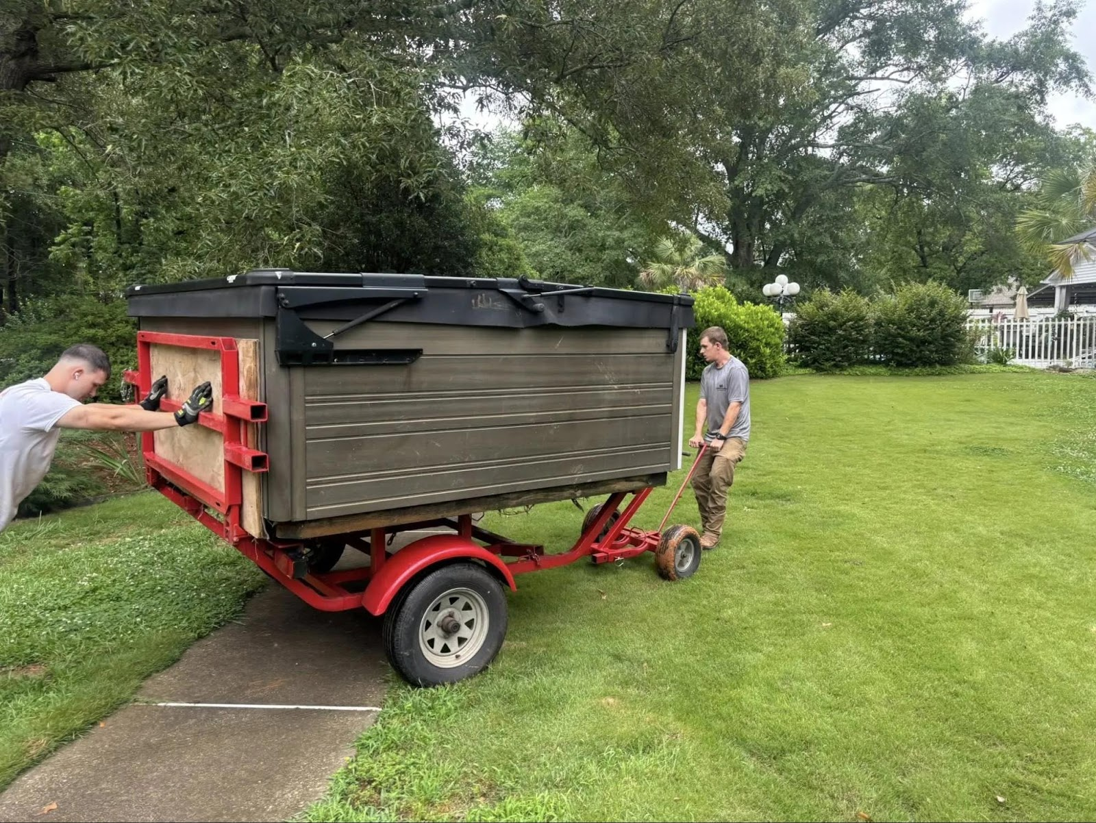 Two men moving a hot tub on a trailer across a lawn. One pushes, one pulls.