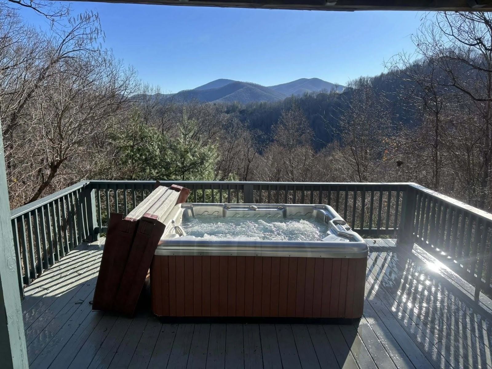 Wooden deck with a hot tub overlooking a mountain view on a sunny day