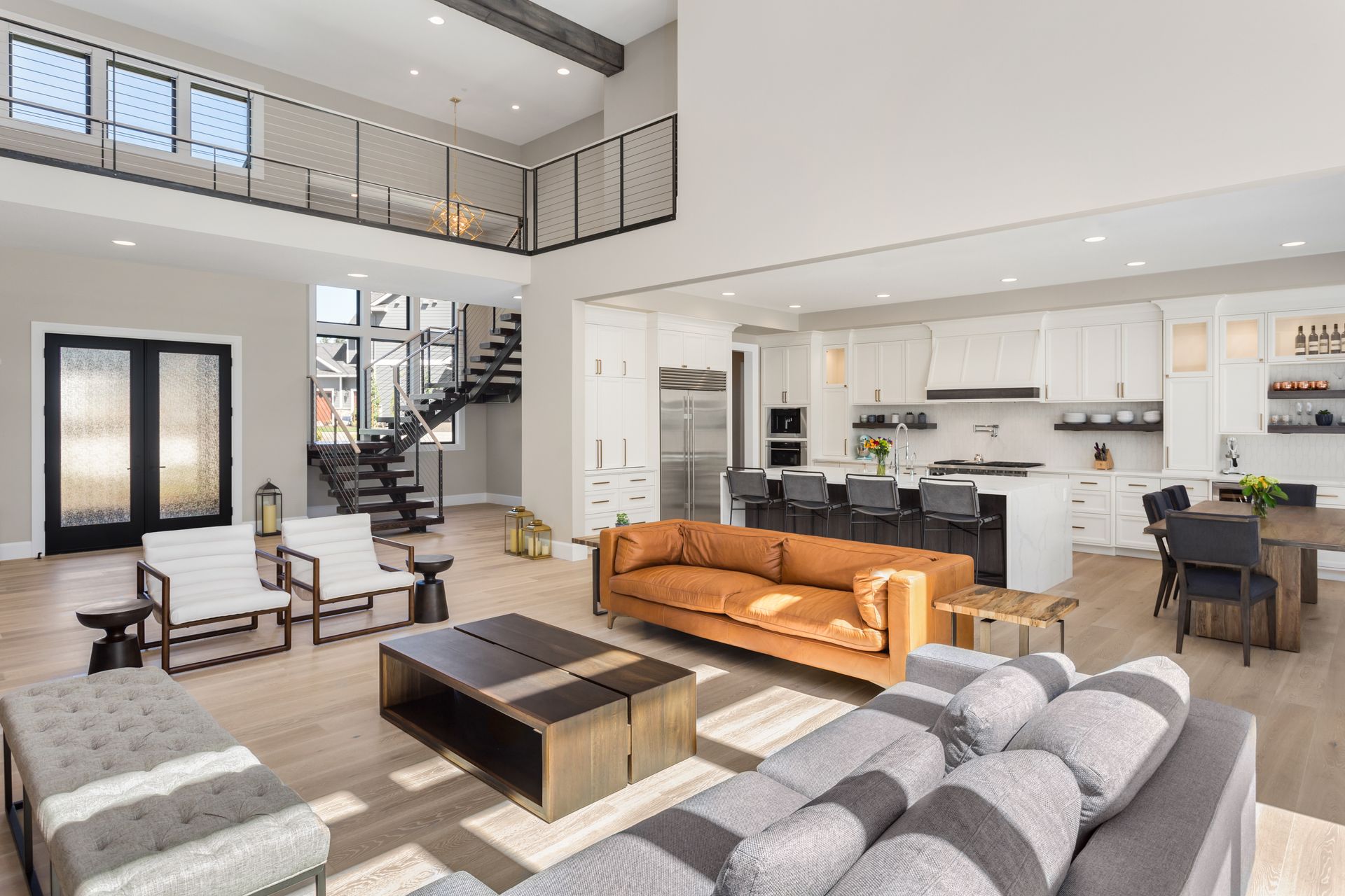 An open-concept living area with a brown leather sofa, white chairs, kitchen island, dining set, and mezzanine staircase.