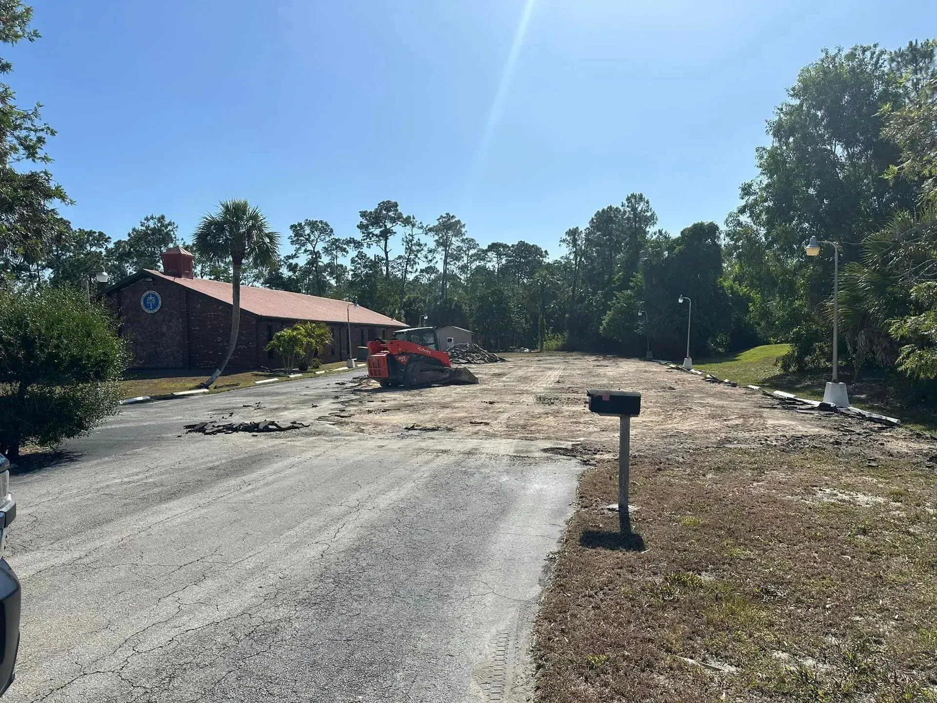 Construction site. A house with a red roof, trees, and a gravel driveway under a blue sky.