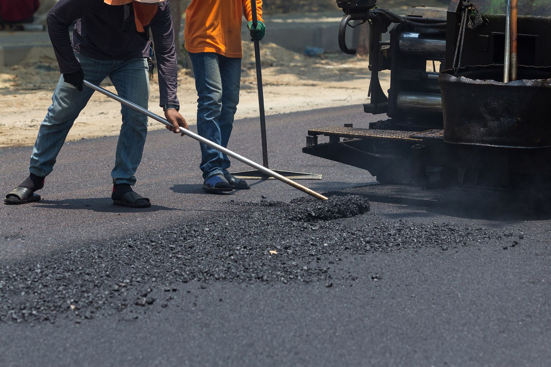 Road workers using tools to spread asphalt on a road.