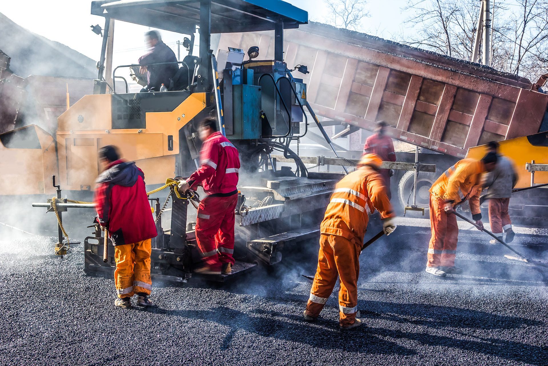 Road construction crew paving asphalt. Yellow paver, dump truck unloading, workers in safety gear.