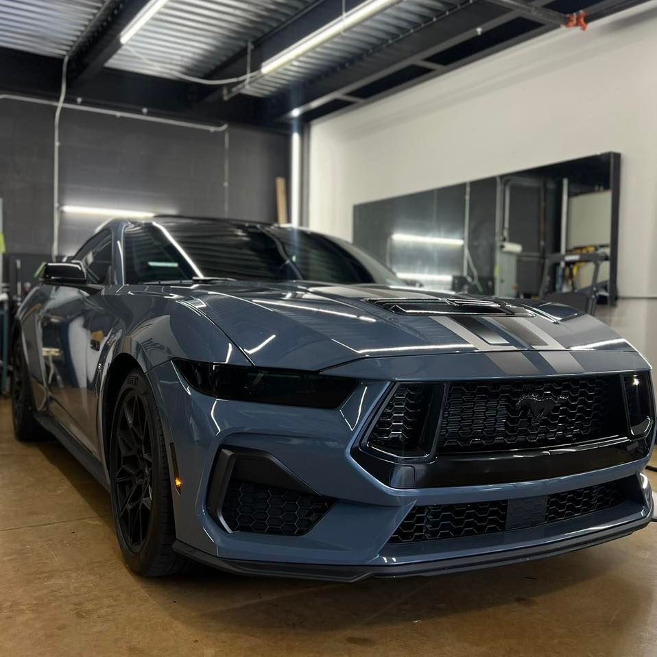 A blue car with black stripes is parked in a garage